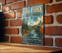 A vintage-style sign for Big Fork State Forest in Minnesota, featuring a scenic illustration of a river surrounded by pine trees and mountains.