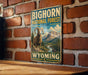 A vintage-style metal sign for the Big Horn National Forest in Wyoming, featuring a large image of a rams against a mountain landscape.