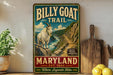 A vintage-style metal sign for the Billy Goat Trail in Maryland, featuring a mountain goat on a rocky cliff with a river below.