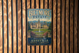 A vintage-style metal sign for Biltmore Estate in Asheville, North Carolina, featuring an illustration of the estate's architecture and landscaping.