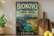 A vintage-style metal sign displaying the name "BIOKOVO IMOTSKI LAKES PARK" and the word "CROATIA" in bold letters, with a scenic image of a lake and mountains in the background.