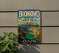 A vintage metal sign displaying the name "BIOKOVO IMOTSKI LAKES PARK" and the word "COTIA" in the bottom right corner, with a scenic image of a lake surrounded by mountains in the background.