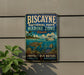 A vintage-style metal sign for Biscayne National Park's Marine Zone, featuring a turtle, fish, and coral reef illustration, along with the text "PROTECT OUR WATERS EXPLORE PRESERVE".