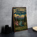 A vintage-style metal sign for Bitterroot National Forest, featuring a mountain landscape with pine trees, a river, and wildflowers.