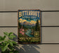 A vintage metal sign for Bitterroot National Forest, featuring a scenic mountain landscape with pine trees, flowers, and a river.