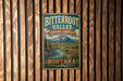 A vintage-style metal sign for Bitterroot Valley Heritage Landscape in Montana, featuring a scenic mountain landscape with a river and pine trees.