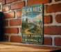 A vintage-style sign for the Black Hills National Forest, featuring a scenic mountain landscape with a lake and pine trees.