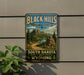 A vintage-style sign for the Black Hills National Forest, featuring a scenic mountain landscape with a winding road and pine trees.