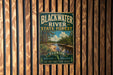 A vintage metal sign for Blackwater River State Forest in Florida, featuring a scenic image of the river surrounded by pine trees and a cloudy sky.