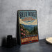 A vintage-style sign for the Blue Ridge National Heritage Area in North Carolina, featuring a mountain landscape and the text "The mountains are calling North Carolina".