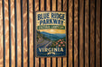 A vintage-style metal sign for Blue Ridge Parkway, featuring a scenic mountain landscape with a winding road and flowers.