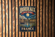 A vintage metal sign for the Bordeaux Port of the Moon in France, featuring a night scene with a full moon, boats, and buildings.