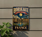 A vintage metal sign with the text "Bordeaux Port of the Moon" and "FRANCE" is displayed on a wall, with a plant to the left.
