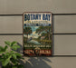 A vintage-style metal sign for Botany Bay Plantation Heritage Preserve, featuring a scenic illustration of a bird, palm trees, and a house along a river.