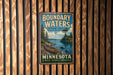 A vintage-style metal sign with a canoe and a scenic landscape, mounted on a wooden wall.