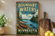 A vintage-style metal sign advertising Boundary Waters, a Minnesota cultural landscape, featuring a canoe on a lake surrounded by pine trees.