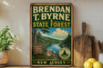 A vintage-style metal sign for the State Forest in New Jersey, featuring a scenic landscape with a river, pine trees, and mountains.