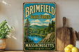 A vintage metal sign for the Brimfield State Forest in Massachusetts, featuring a scenic landscape with a lake and mountains.