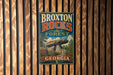 A vintage metal sign for Broxton Rocks Forest in Georgia, featuring a scenic image of a rock formation surrounded by trees and flowers.