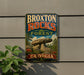 A vintage-style metal sign for the Broxton Rocks Forest in Georgia, featuring a large rock formation and surrounded by trees and flowers.