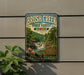 A vintage-style metal sign for Brush Creek State Forest in Ohio, featuring a scenic landscape with a waterfall and lush greenery.