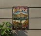 A vintage-style metal sign displaying the name "Budapest" and the words "Budapest, The Pearl of the Danube" is affixed to a wall.