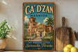 A vintage-style sign for "CA' D' ZAN" mansion in Sarasota, Florida, featuring an illustration of a grand, ornate building surrounded by palm trees.