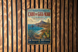 A vintage metal sign with a coastal landscape and text in Spanish, hanging on a wooden fence.