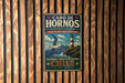 A vintage metal sign with text and an illustration of a lighthouse and a bird, mounted on a wooden wall.