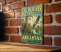 A vintage metal sign for the Cache River National Wildlife Refuge in Arkansas, featuring an illustration of a bird in flight over a marshy area with trees and water.