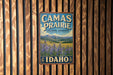 A vintage-style metal sign with the text "Camas Prairie Cultural Landscape Idaho" displayed on a wooden wall.
