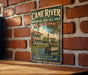 A vintage-style metal sign for the Cane River National Heritage Area in Louisiana, featuring an illustration of a historic building and a boat on the water.