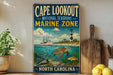 A vintage-style sign for Cape Lookout National Seashore Marine Zone, featuring an illustration of a lighthouse, a turtle, and fish in the ocean.