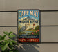 A vintage-style metal sign for the Cape May National Wildlife Refuge, featuring a blue heron and a lighthouse, mounted on a gray wall.
