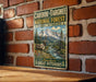 A vintage-style metal sign advertising the Caribbean-Targhee National Forest in Idaho, Wyoming, featuring a mountain landscape with a reindeer.