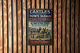 A vintage metal sign with the title "CASTLES AND TOWN WALLS OF KING EDWARD GYNEDD" is displayed on a wooden wall.