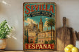 a vintage metal sign with the text "SEVILLA CATEDRAL ALCAZAR ARCHIVO DE INDIAS" and "ESPAÑA" on it, depicting a cityscape with a cathedral and palm trees. The sign is placed on a shelf next to a wooden cutting board and a potted plant.