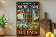 A vintage-style metal sign advertising the Cathedrale de Notre-Dame in Paris, France, featuring images of the cathedral and surrounding buildings.