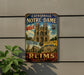 A vintage metal sign advertising the Cathedra de Notre-Dame in Paris, France, featuring the cathedral's spires and surrounding architecture.