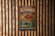 a vintage-style metal sign with a wooden background, advertising the "CAVE OF ALTAMIRA" and the "PALEOLITHIC CAVE ART".