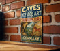 a vintage-style sign with the text "CAVES and ICE AGE ART in the SWABIAN JURA in GERMANY" displayed on a brick wall.