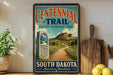 a vintage trail sign for the Centennial Trail in South Dakota, with a scenic mountain landscape and a path leading through the grassy area.