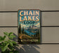 A vintage-style metal sign for Chain Lakes Loop in Washington, featuring a scenic mountain landscape with pine trees and a lake.