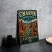 A vintage-style metal sign for Charyn Bioscape Reserve, featuring a desert landscape with mountains and a river, is displayed on a gray countertop next to a stack of black camera lenses.