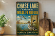 A vintage-style metal sign for the Chase Lake National Wildlife Refuge in North Dakota, featuring an illustration of ducks and a sign that says "A Haven for Wildlife".