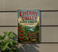 A vintage-style metal sign for Cherry Valley State Forest in New York, featuring a scenic landscape with cherry trees and a river.