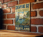 A metal sign with text and an illustration of a bird and a body of water, mounted on a brick wall.