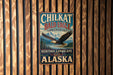 A metal sign with the text "CHILKAT BALD EAGLE PRESERVE HERITAGE LANDSCAPE ALASKA" is displayed on a wooden wall.
