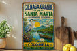 A vintage-style metal sign advertising the Cienaga Grande de Santa Marta Biosphere Reserve in Colombia, featuring a blue heron, a canoe, and a scenic landscape.