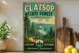 A vintage-style sign for Clatsop State Forest in Oregon, featuring a scenic landscape with pine trees, mountains, and a beach.